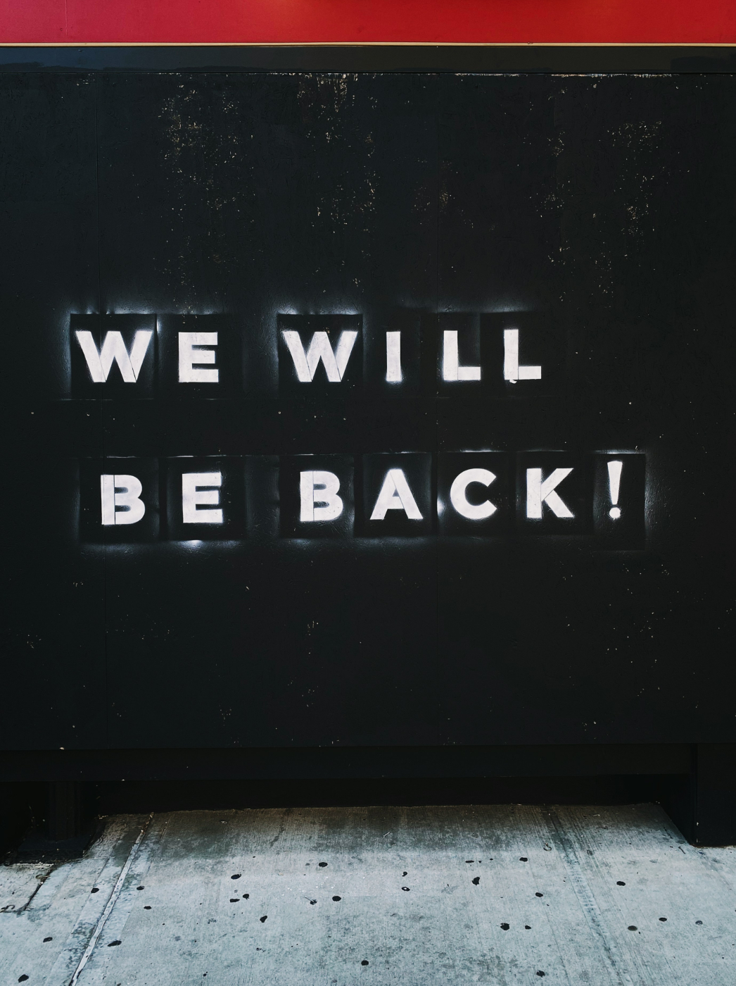 Stenciled white words on a black wall reading WE WILL BE BACK!