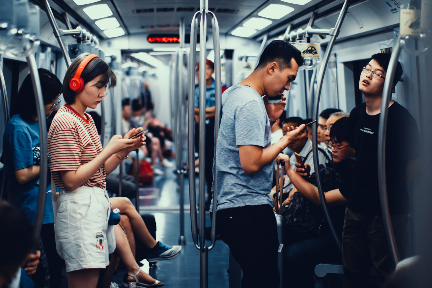 A subway car, everyone is on their phone except for one guy who's asleep standing up