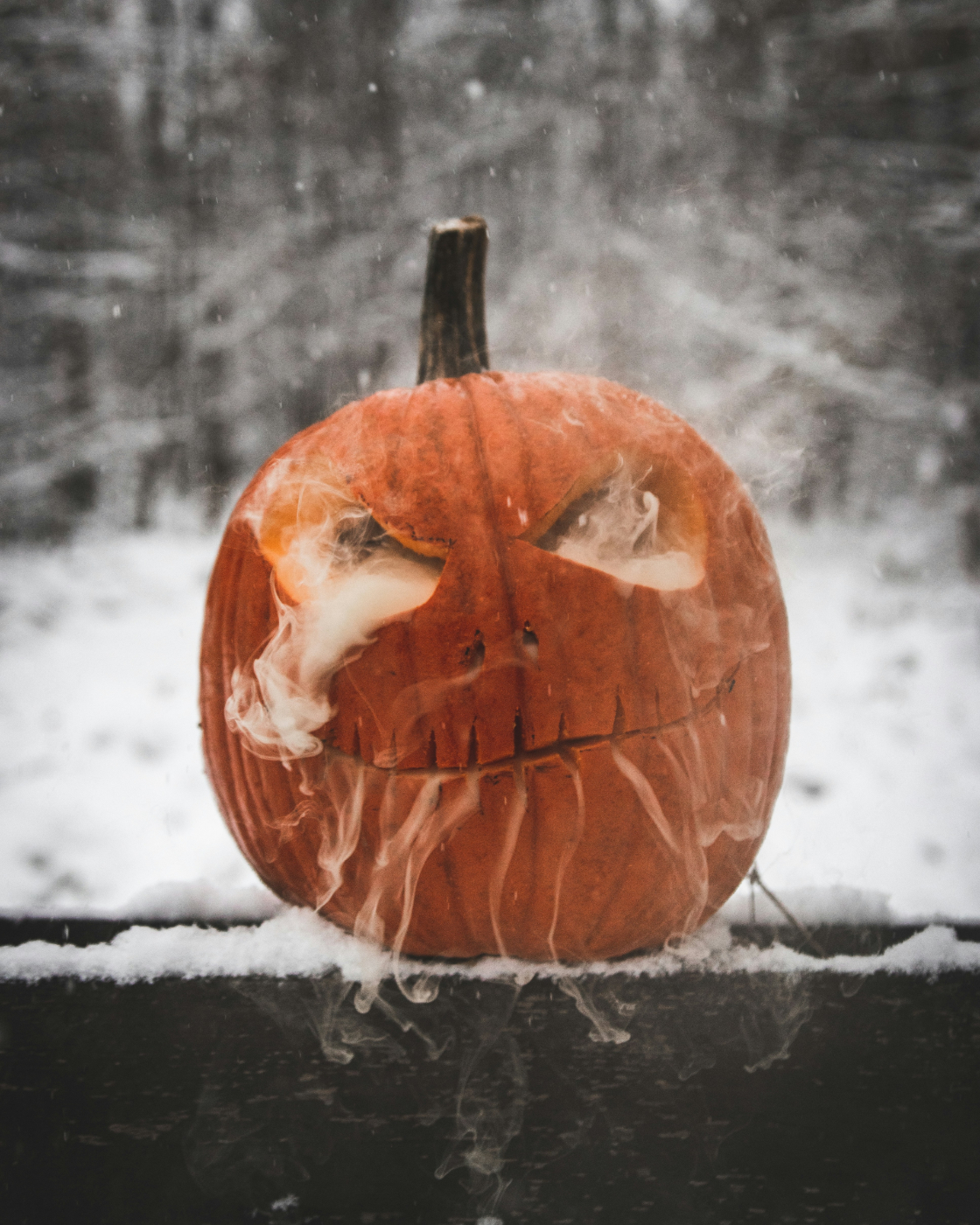 a carved pumpkin with smoke coming from its eyes and mouth against a snowy background