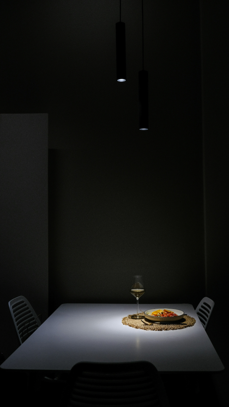 A dark room with downlights on a spare table with a setting for one