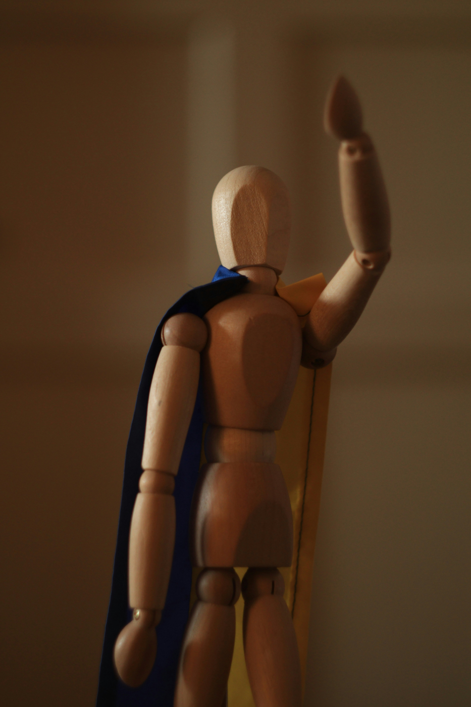 An artists mannequin wearing a blue cape and waving