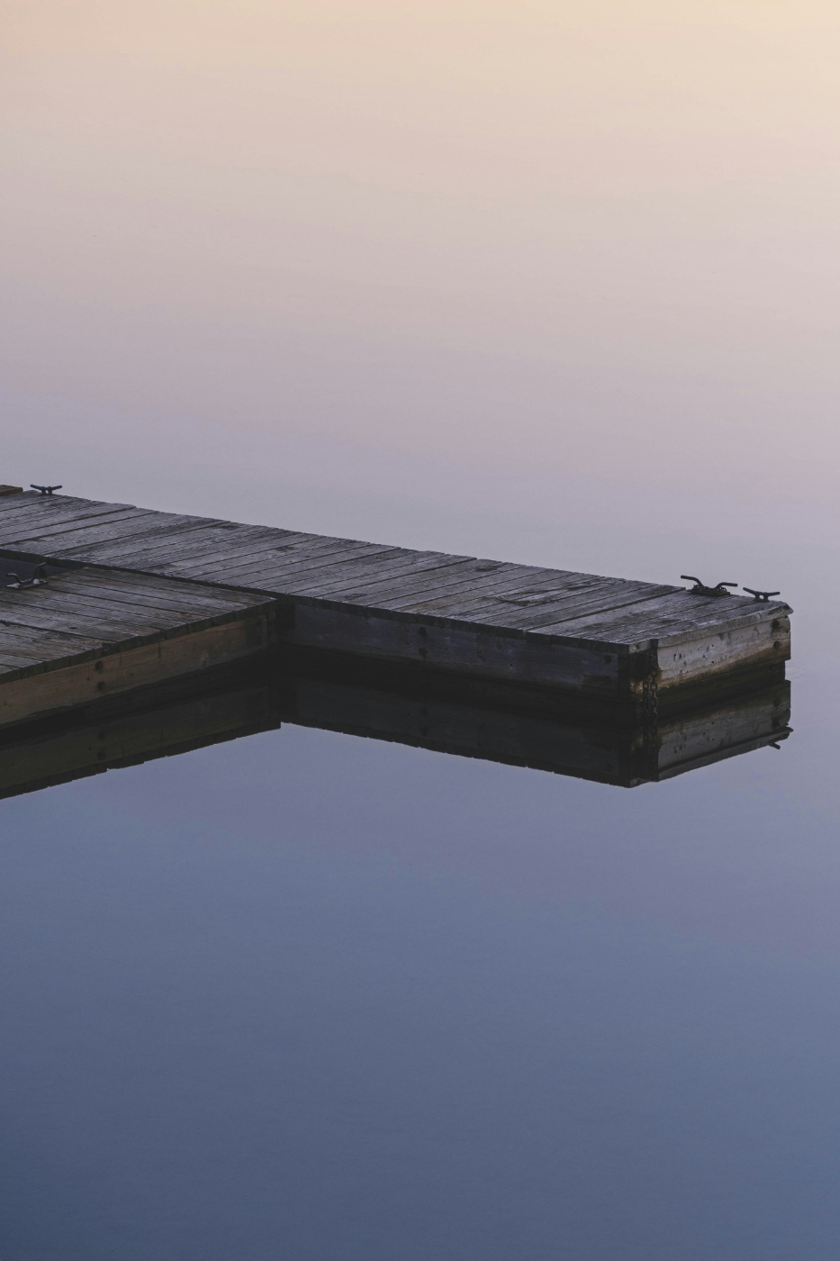 A wooden dock on a dead calm lake at dusk