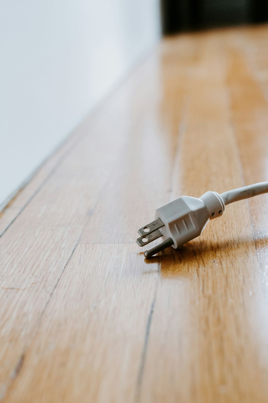 A 3 prong plug removed from the socket laying on a wood floor