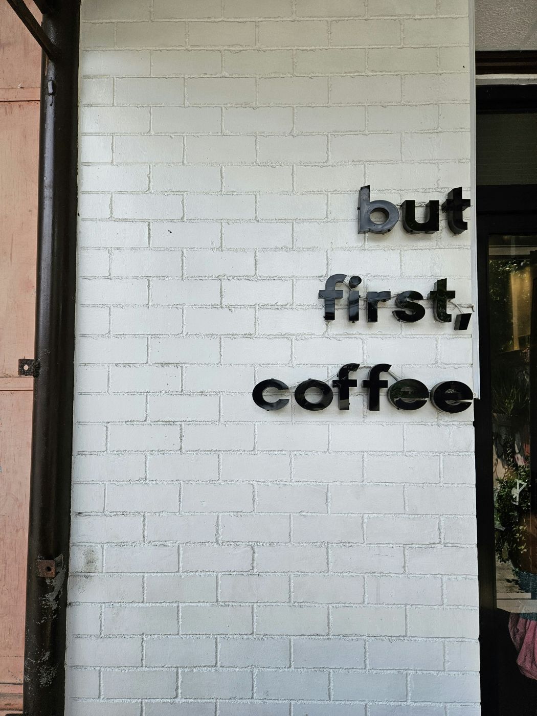 A white brick wall with But First Coffee in black letters