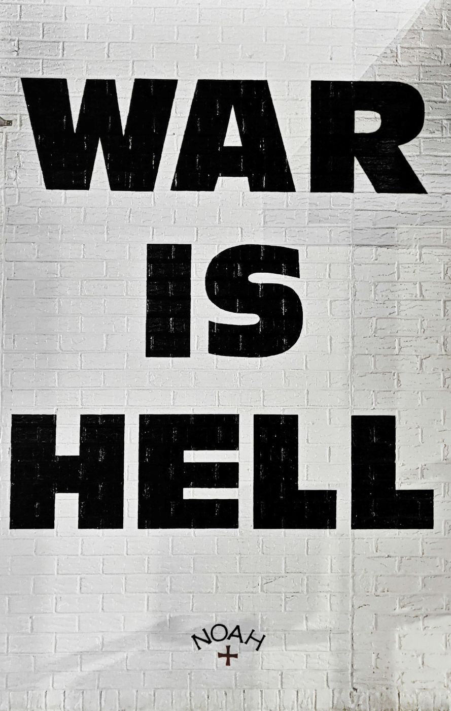 A white painted brick wall with War Is hell in huge black block letters