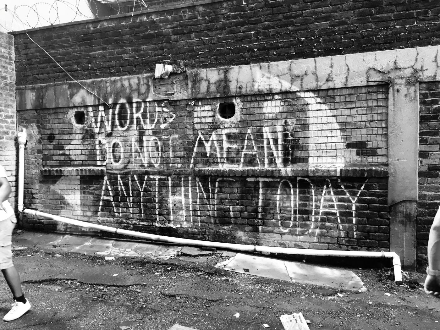 Black and white of graffiti on a brick wall reading Words Do Not Mean Anything Today