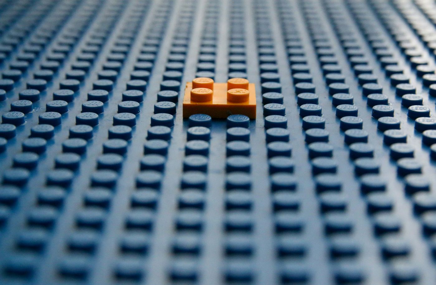 An orange Lego brick on a large blue Lego plain
