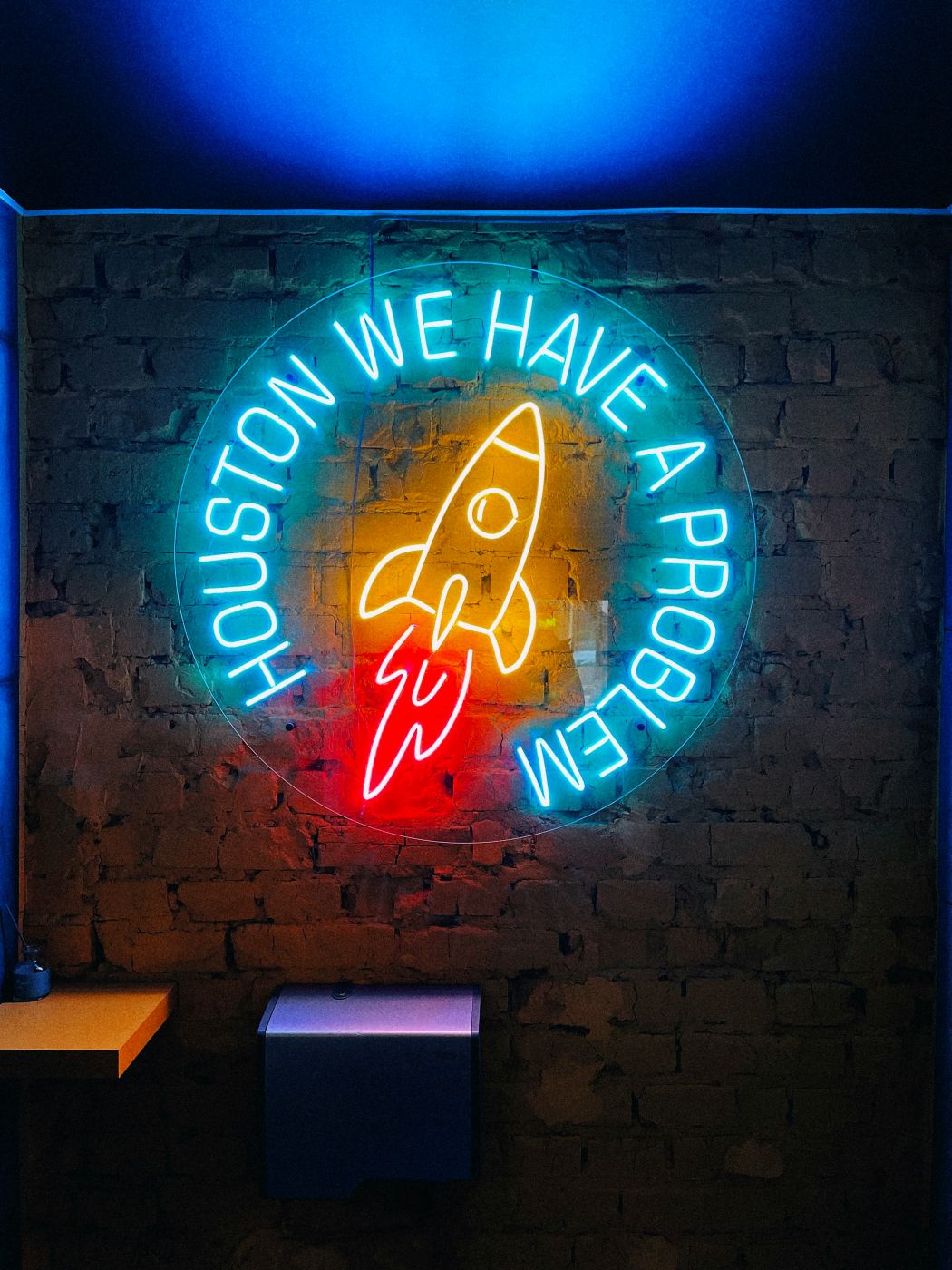 A colorful neon sign with a yellow rocket, red flames and the words Houston We Have  Problem