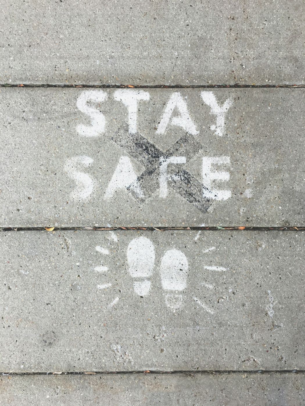 White letters stenciled on a sidewalk reading Stay Safe with two shoe prints