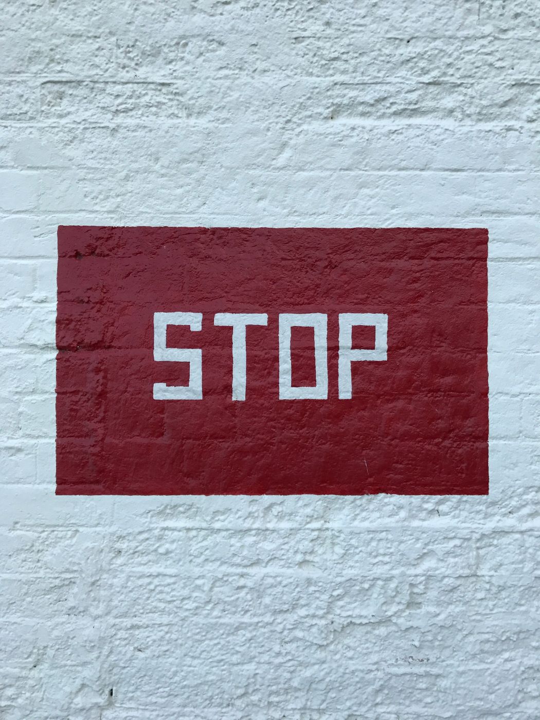 A red rectangle with white letters in it spelling stop on a white wall