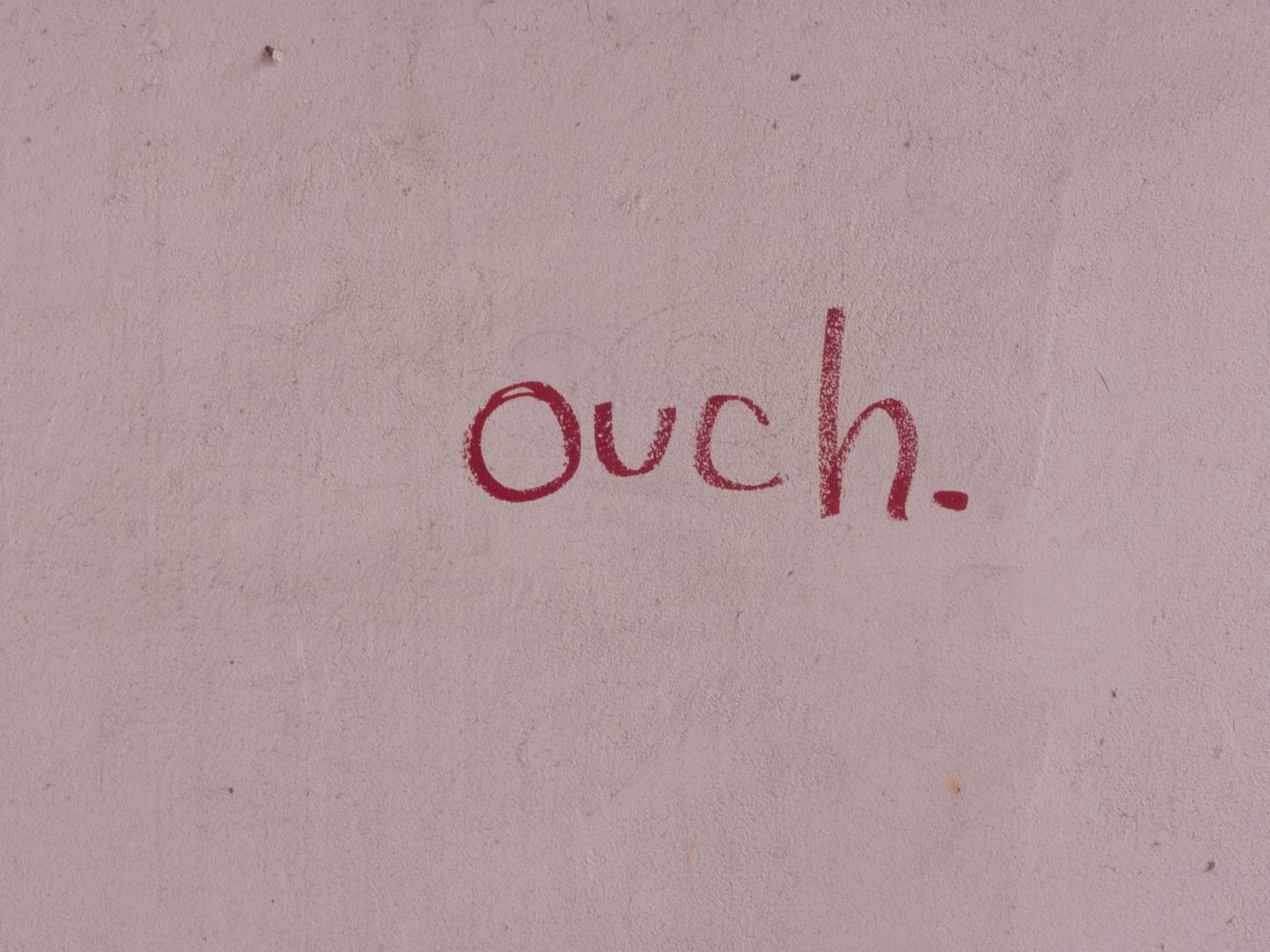 A pinkish wall with the word ouch written on it in red lipstick