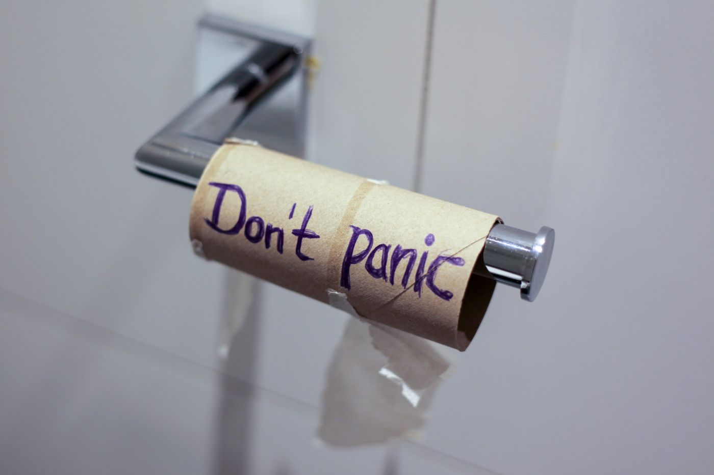 An empty toilet paper roll on the rack with don't panic written on it in purple
