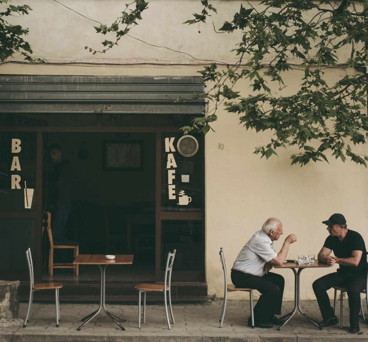 Two men having a conversation at a table outside a cafe