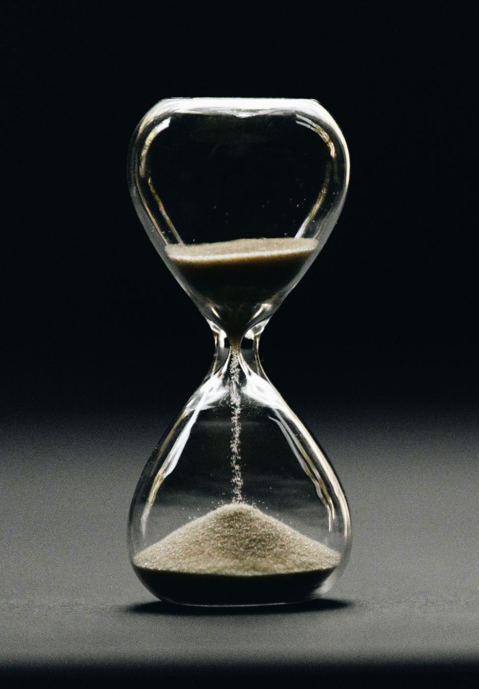 A glass sand timer on a grey table against a black background