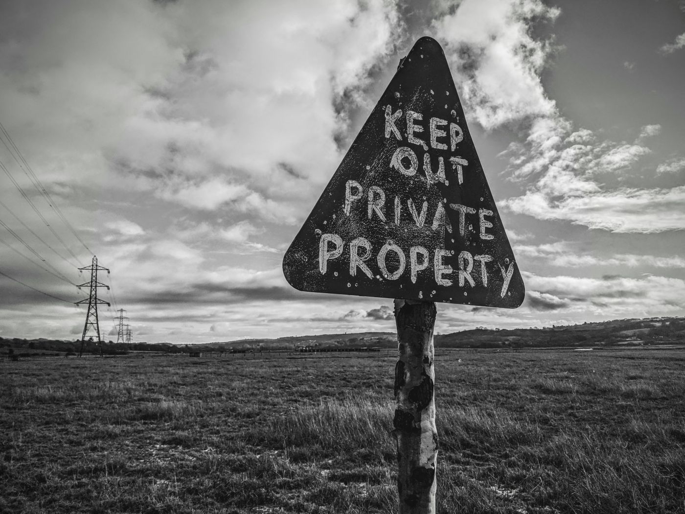 Black and white shot of a triangular sign in a field reding Private Property Keep Out