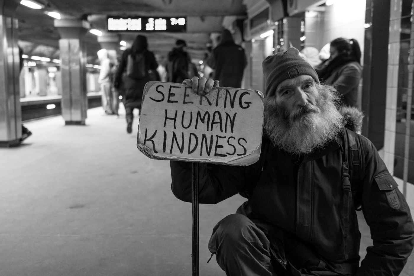 A bearded man holding a sign reading Seeking Human Kindness
