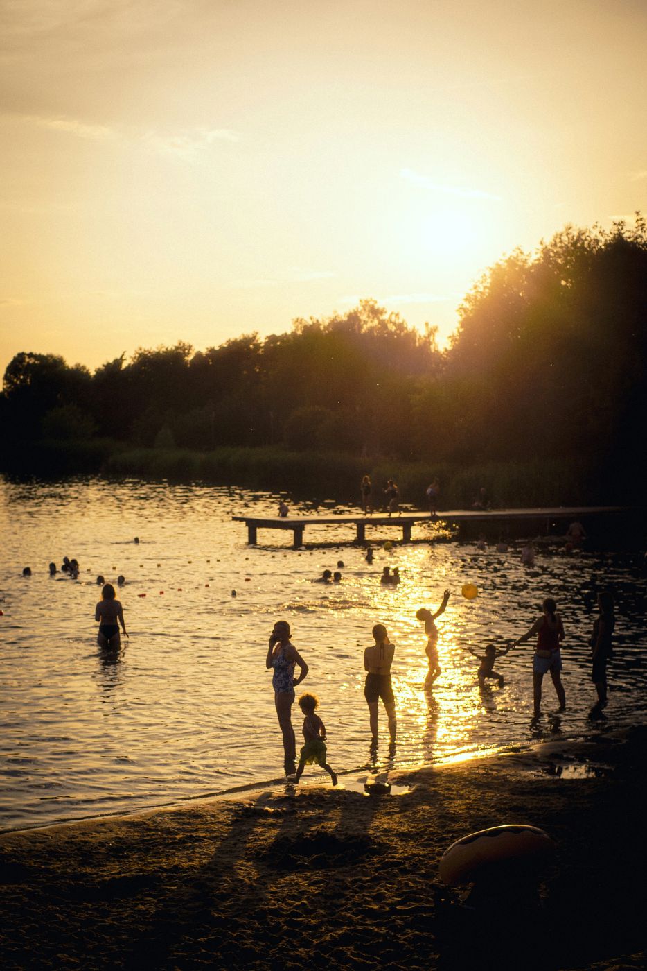 People playing on a beach near a lake at sunset