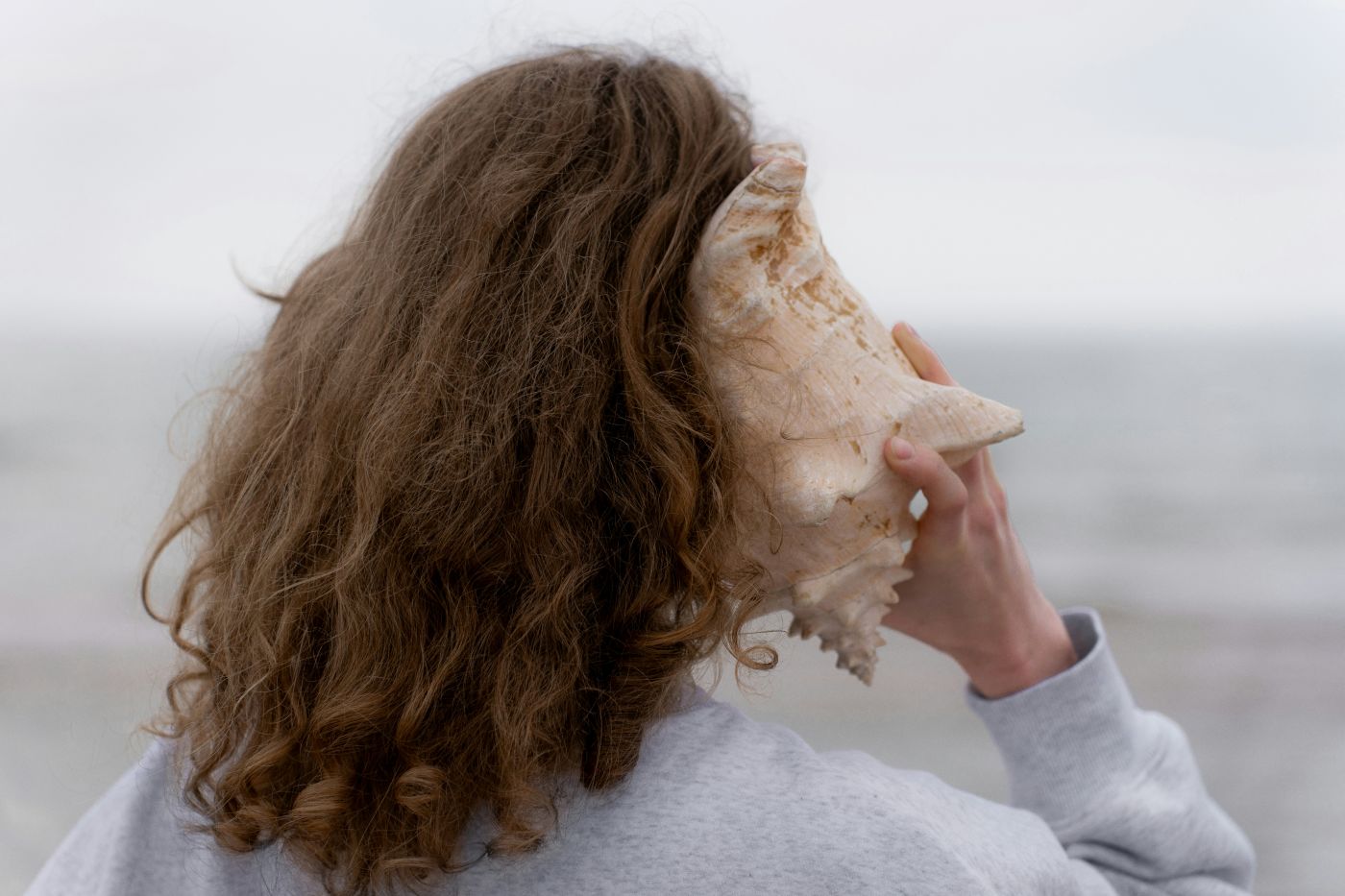 From behind a woman holding a conch shell to her ear