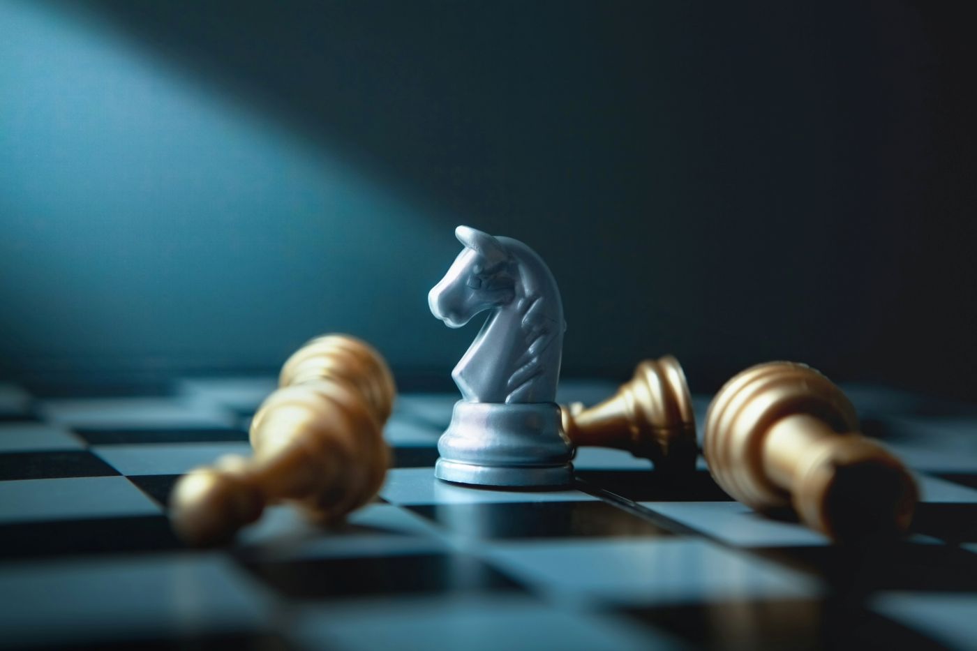 A white knight chess piece surrounded by three toppled pawns and one toppled Rook