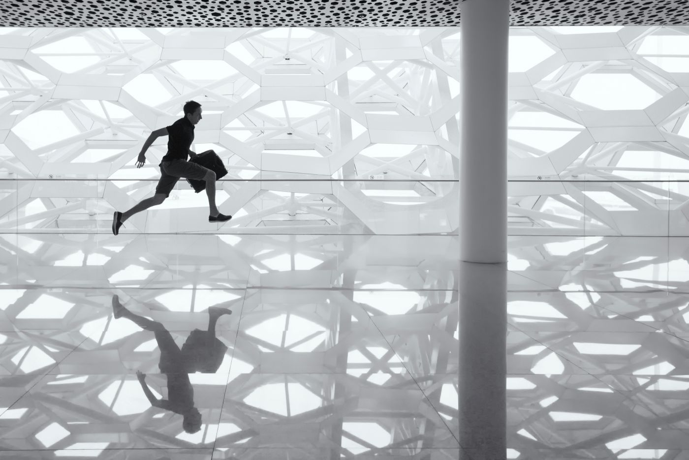 A man with a suittcase running across a reflective floor in an airport