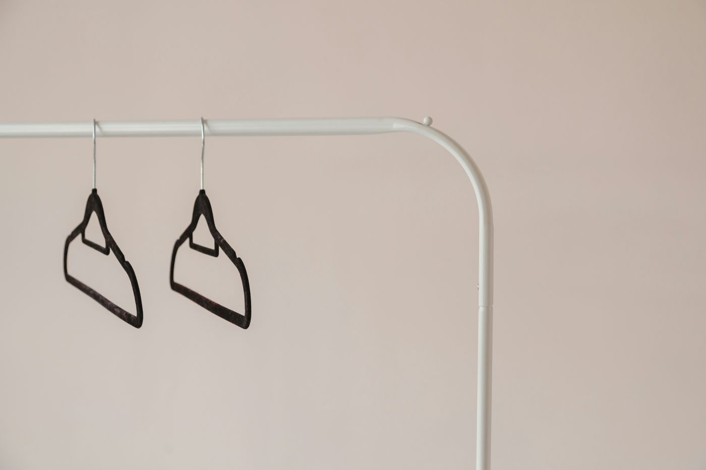 Two empty black hangers on a white rack