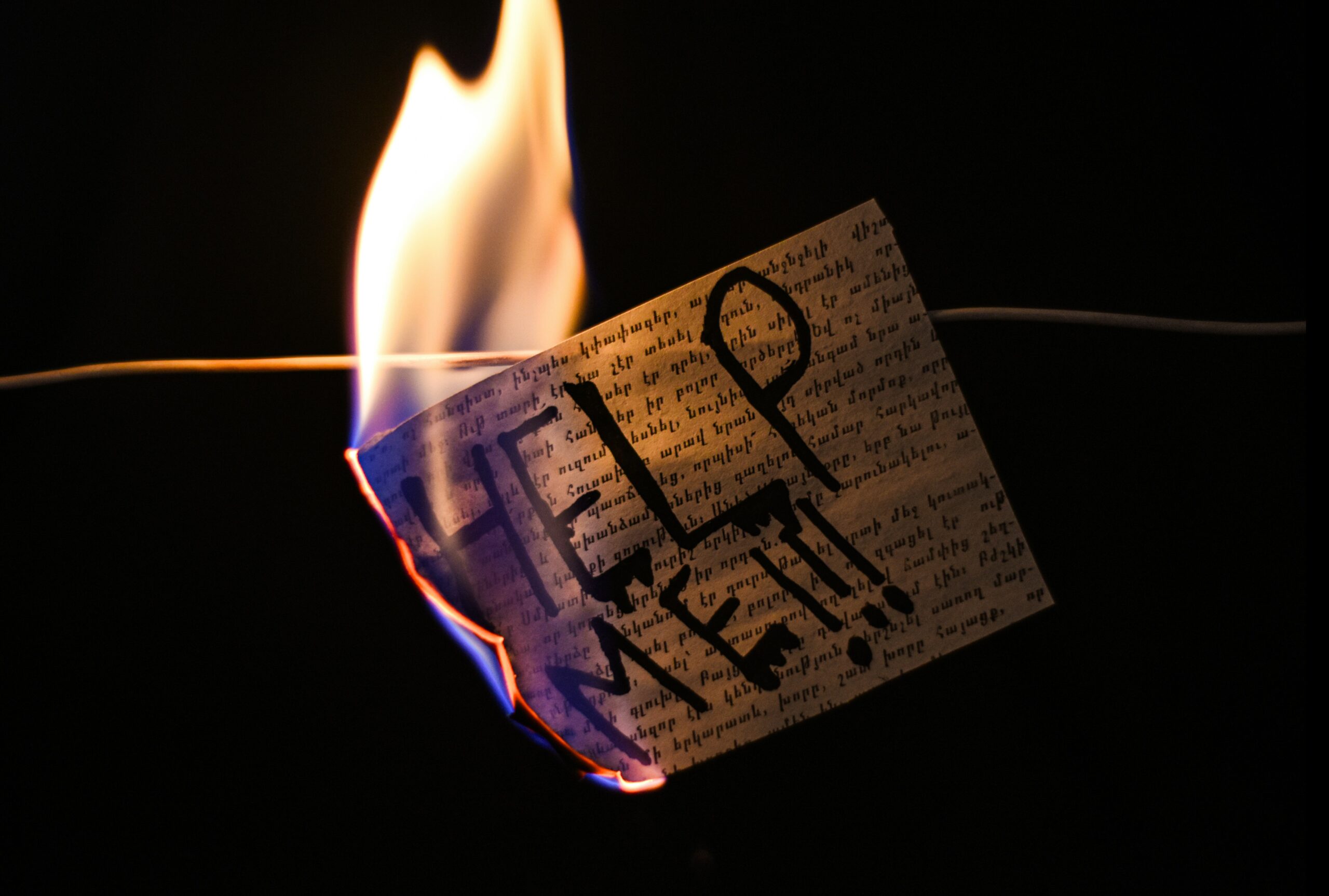 A post card with Help Me!!! Written on it, on a line on fire.