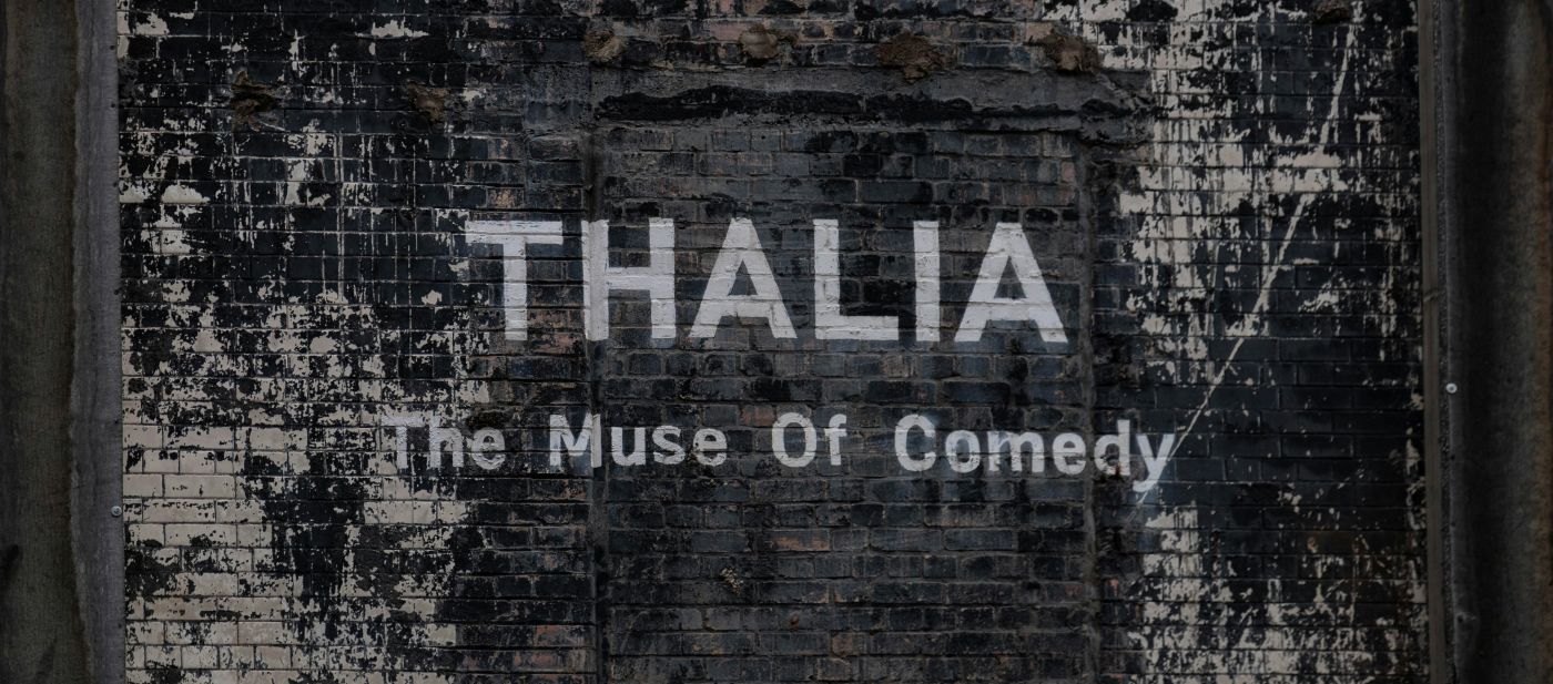 A black and white brick wall with Thalia, the Muse of Comedy, painted on it