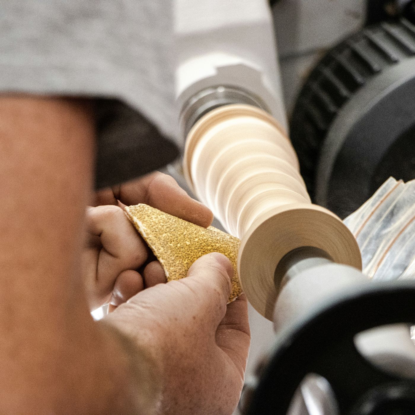 A person sanding a turned piece of wood on a lathe