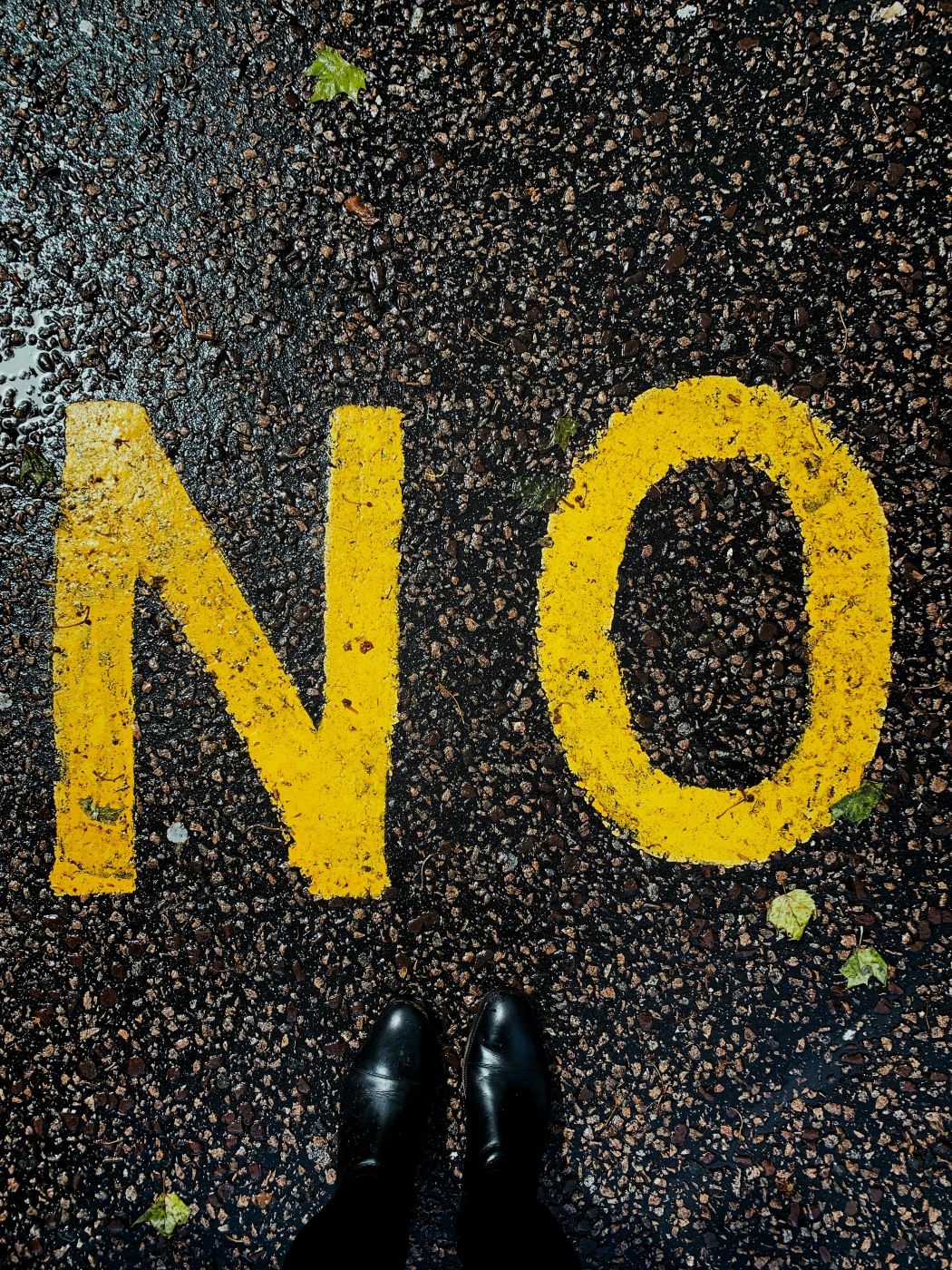 NO painted in yellow on a black street with a pair of black shoes in the frame