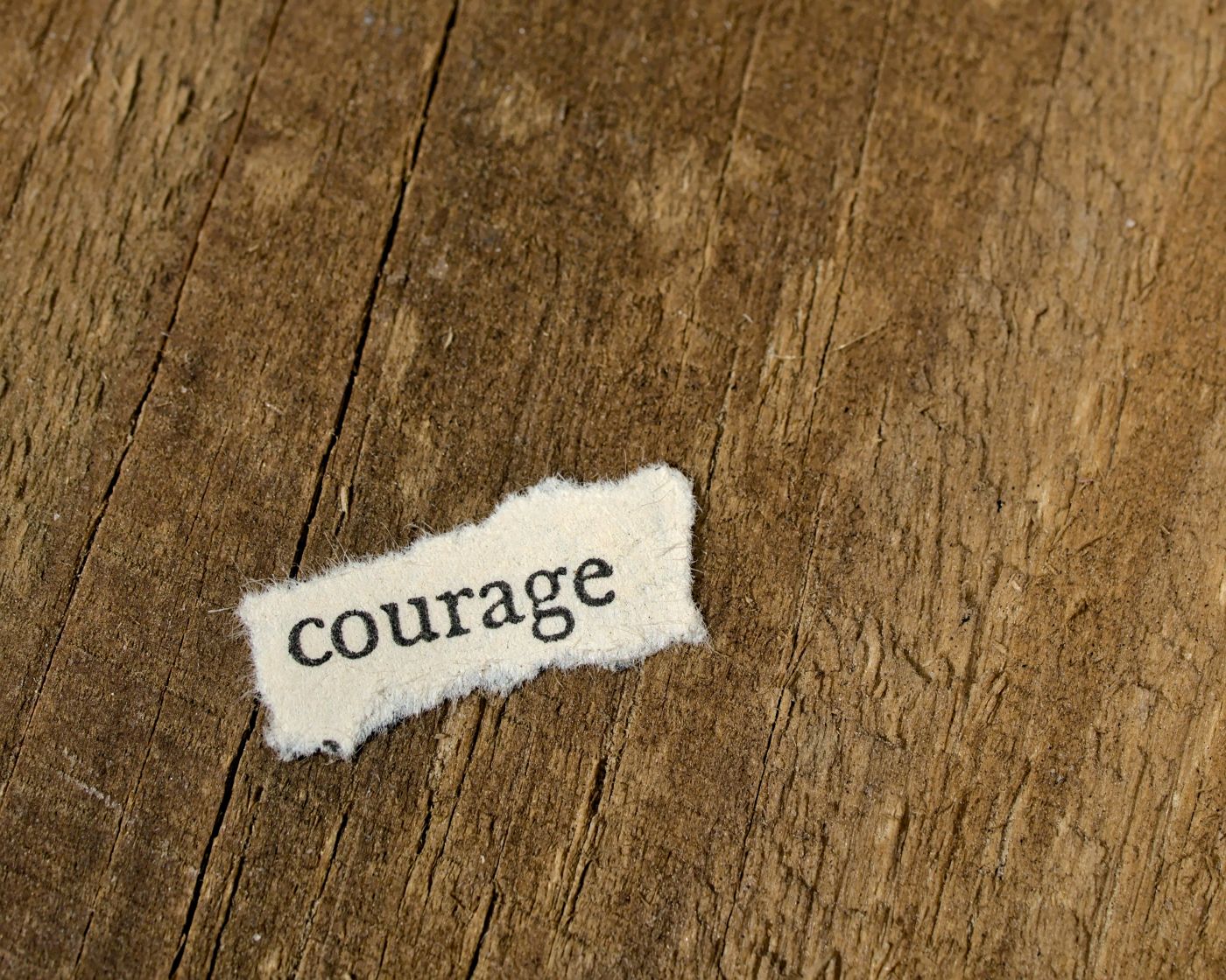 a small scrap of paper on a wooden table that has the word courage printed on it