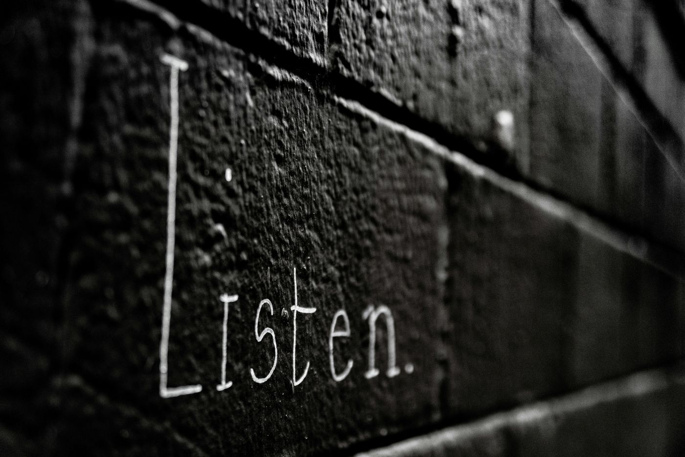 A black painted brick wall with the word Listen written in white.