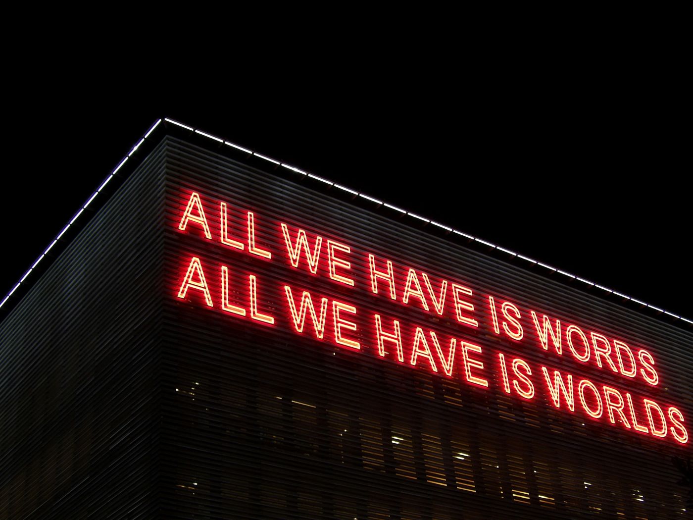 Red neon sign on the side of a building reading: All we have is words. All we have is worlds