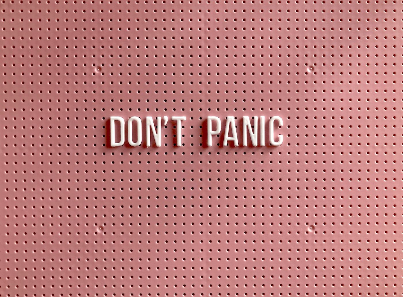 A pink peg board with pale pink letters reading Don't Panic