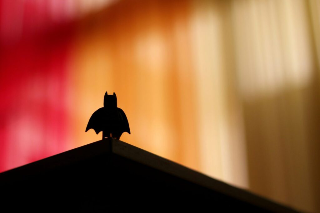 silhouette of Lego Batman standing on the corner of a desk with a blurred, multi-colored background