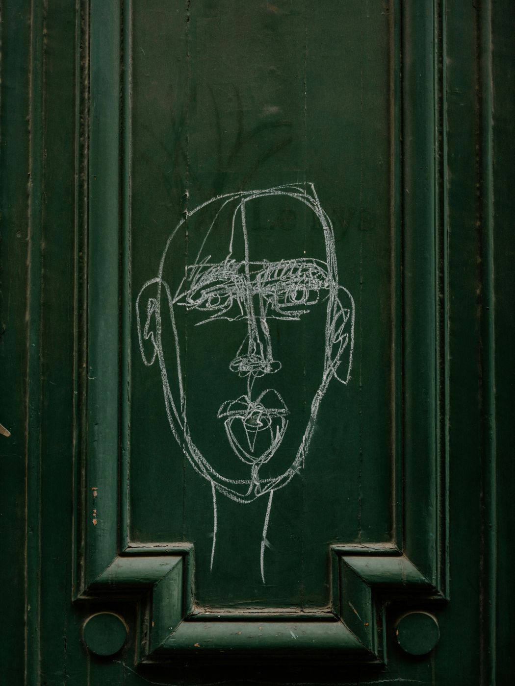 a white chalk drawing of a man's face on a green door