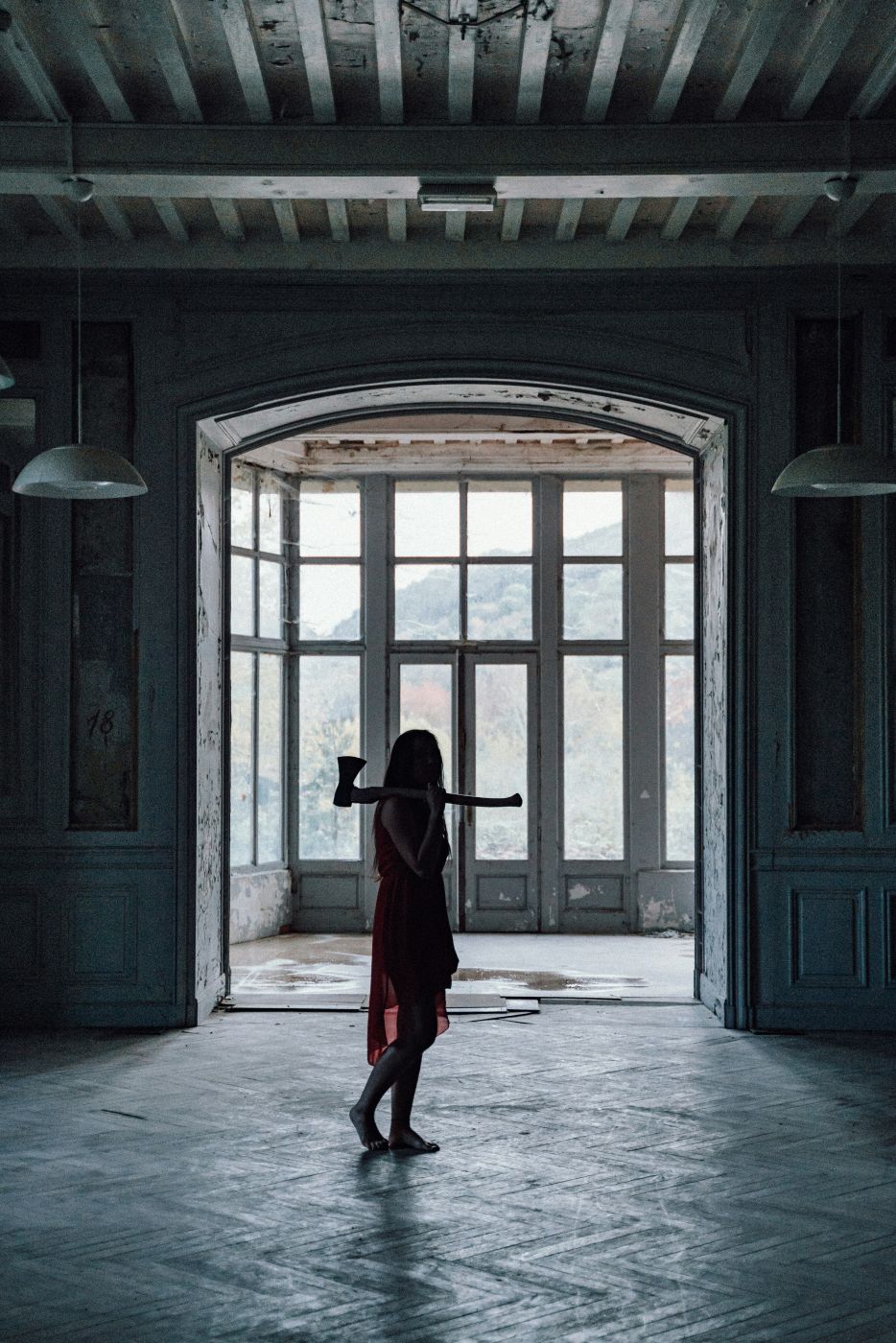 An abandoned house with a girl in a red dress carrying and axe