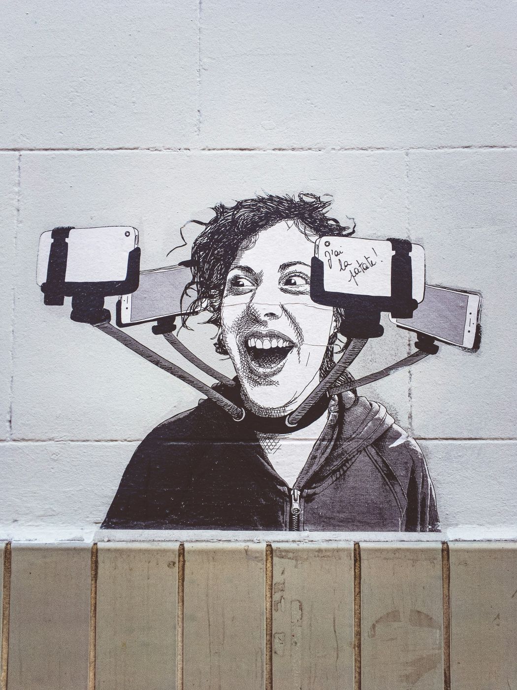 A graffiti image on a wall of a man with a collar of cell phones all pointing at himself