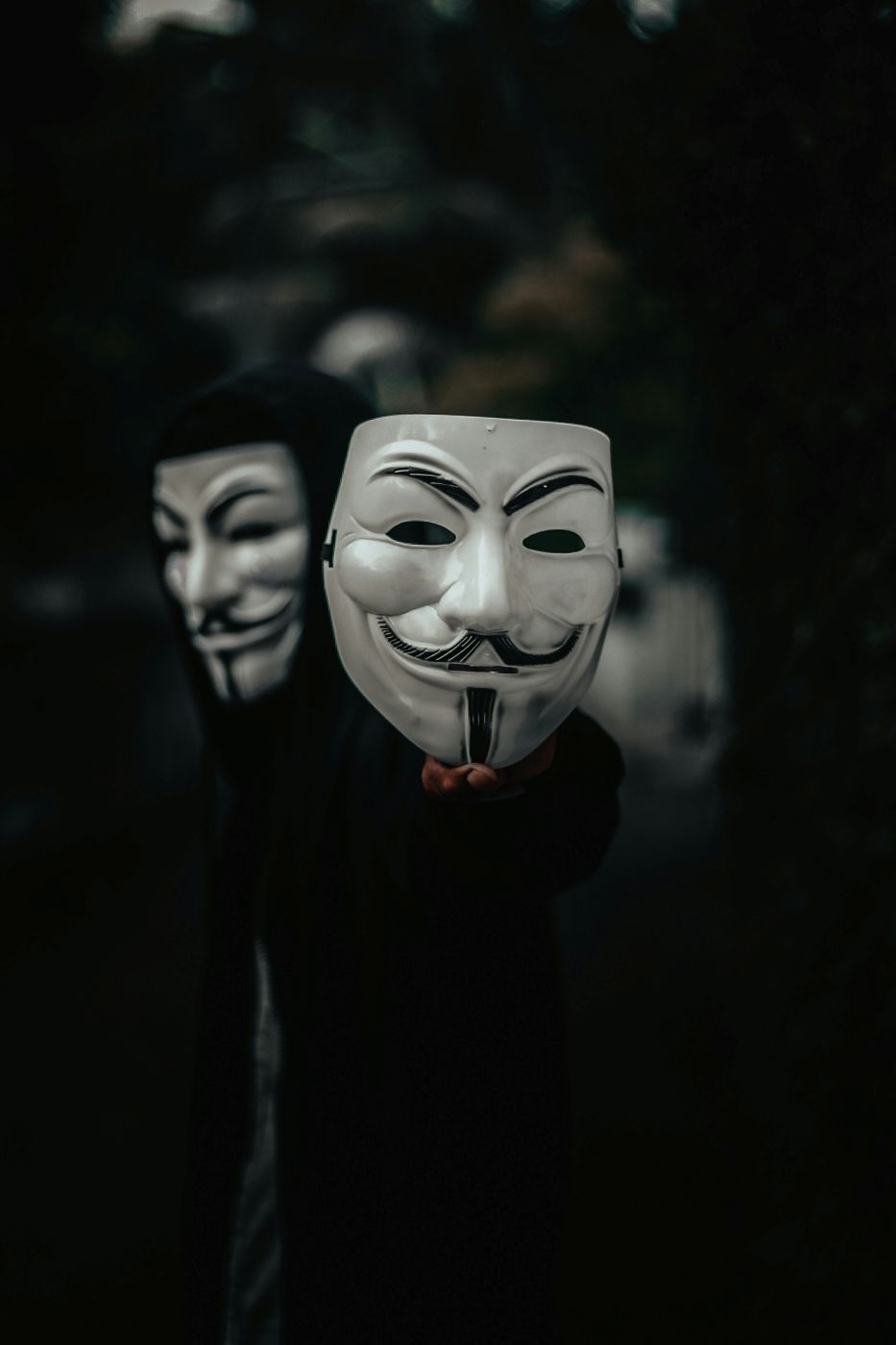 A man wearing and holding up a Guy Fawkes mask