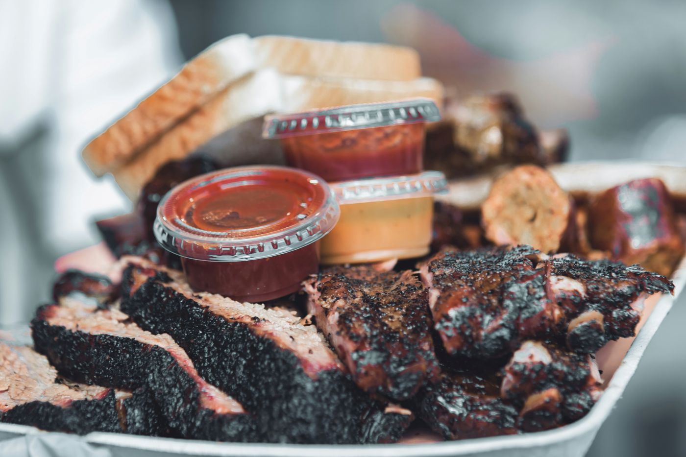 A plateful of BBQ ribs, bread, sauces, and fries